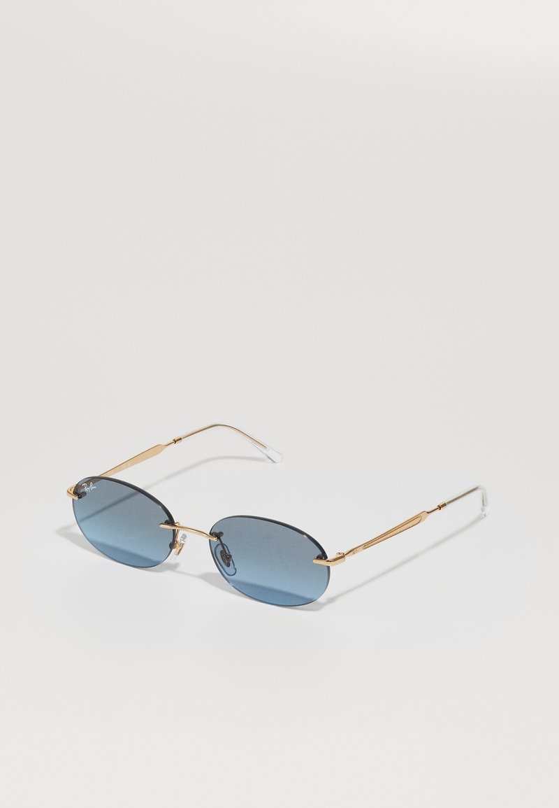 Gafas de sol con lentes ovalados de tono azul, montura de metal dorado, patillas delgadas y puntas de oreja de plástico transparente. Diseño minimalista con acentos estrechos.