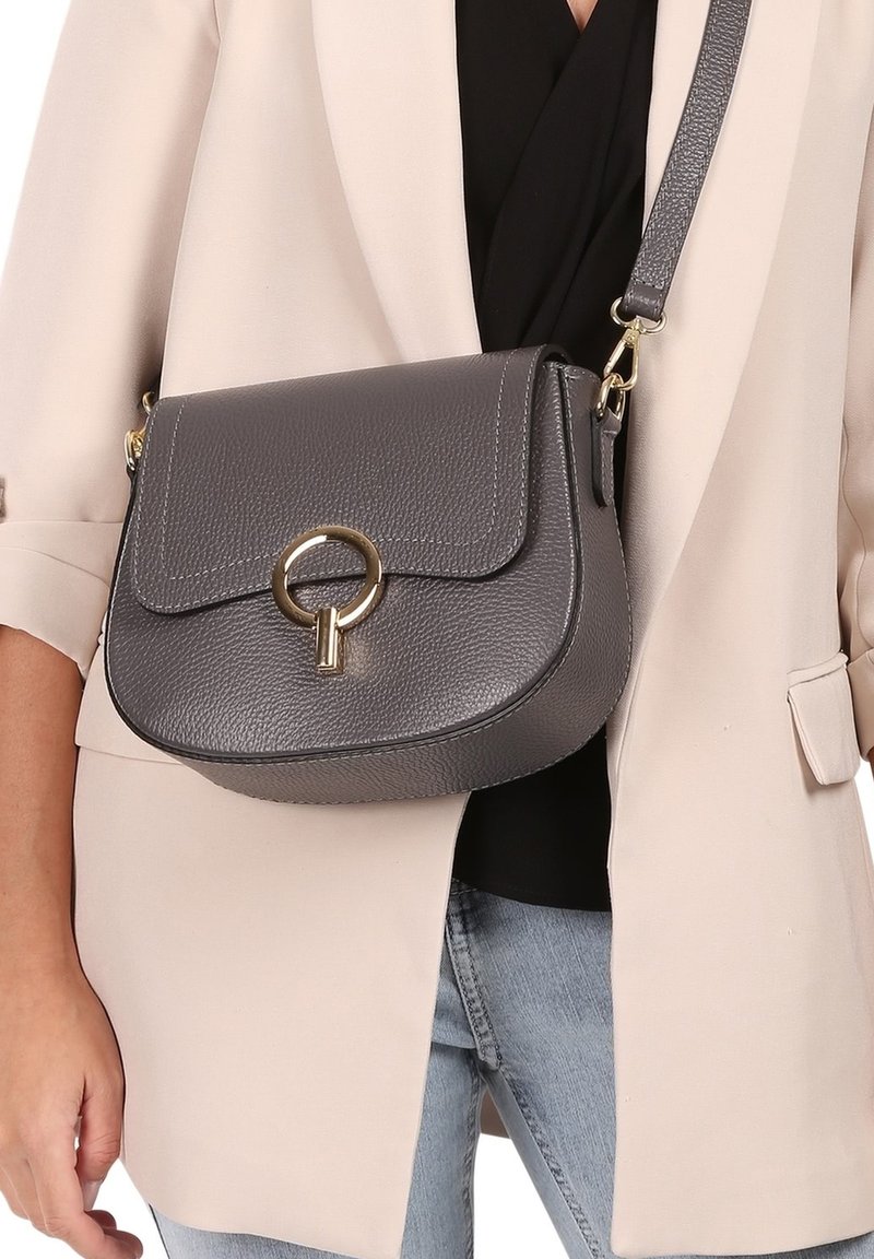 Gray leather crossbody bag with a rounded shape, a flap closure, gold hardware, and a circular accent detail. Adjustable strap included.