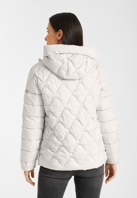 Lichtgrijze pufferjack met capuchon, voorzien van een ruitpatroon, een gladde textuur en elastische manchetten. De achterkant toont een lichte tailleversmalling.