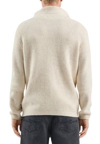 Roomkleurige, geribde trui met een sjaalkraag en lange mouwen, gemaakt van zacht materiaal. Heeft een klein merkje aan de zijkant.