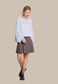 Lyseblå gjennomsiktig bluse med rynket hals, kombinert med en brun plisserte skjørt. Modellen har på seg svarte sko og stripete knesokker.