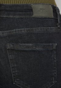 Jeans de denim azul oscuro con una textura suave. Presentan un bolsillo trasero y una etiqueta que dice "ONLY". Detalles de costura simple en los bordes.