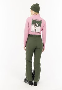 Roze langarmtop met grafische print op de achterkant en groene sneeuwbroek. Kenmerkt zich door een getailleerd ontwerp en zwarte accenten op de broekspijpen.
