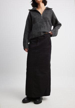 Grå ribstrikket sweater med zipkrave, kombineret med et langt sort skørt med sømdetaljer og flade lommer. Sorte chunky støvler fuldender outfittet.