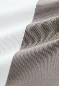 Mintás szövet váltakozó fehér és világosbarna csíkokkal. A felület szövött mintázatú, tapintható textúrát kölcsönözve neki.