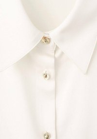 Camicia bianca con colletto classico e bottoni dorati lucidi. Tessuto dalla texture liscia, con tre bottoni frontali.