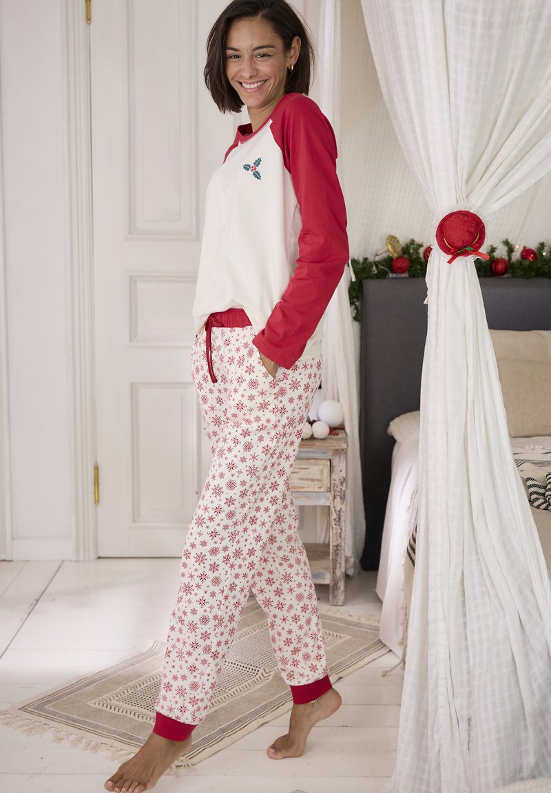 Rode en witte pyjama set met een top met een gebogen zoom, rode mouwen en een geborduurd ontwerp. De broek heeft een sneeuwvlokpatroon en rode boorden.
