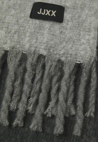 Écharpe en laine grise à finition texturée, avec des bords frangés et une étiquette noire avec du texte blanc, affichant les lettres "JJXX."