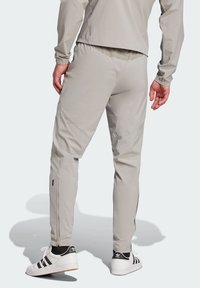 Joggers en gris claro, ajustados y con cremalleras laterales, cintura elástica y costuras en contraste. Combinados con zapatillas deportivas en blanco y negro.