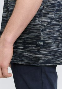 Kortærmet navy T-shirt med et struktureret, stribet mønster i varierende nuancer. Har et label ved sidesømmen og en afslappet pasform.