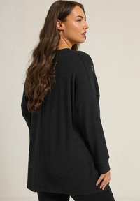 Schwarzer, übergroßer Pullover mit langen Ärmeln, entspannt geschnitten und mit strukturierten Details auf der Rückseite. Aus weichem Strickstoff und mit seitlichen Schlitzen.