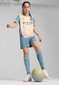 Detský futbalový dres s prechodom od žltej po modrú, zdobený ružovými akcentmi, modré šortky a ponožky po kolená. Biely futbalový kopačky.