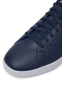 Sötétkék bőr sportcipő, megfelelő színű fűzőkkel, perforált szellőzőnyílásokkal az orr részen, és fehér gumitalppal.