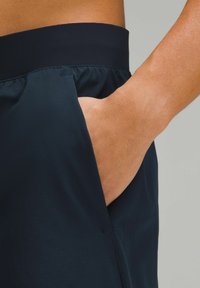 Marineblauwe shorts met een gladde textuur, elastische tailleband en zijvak. Close-up zicht benadrukt de details van het vak en de tailleband.