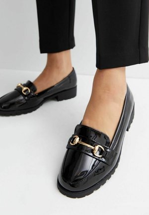 Sorte loafers i laklæder med lav blokhæl og en gylden metalrem tværs over fronten. Glat, blank overflade.
