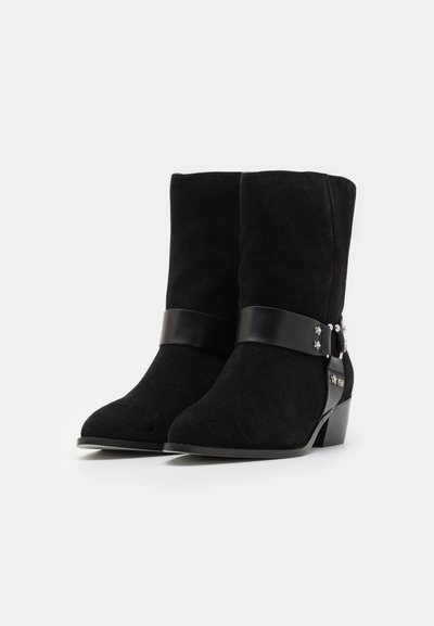 Pair of black suede ankle boots with low heels, leather strap around the ankle, and small silver star and stud embellishments.