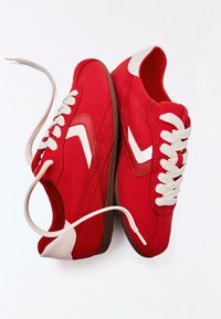 Paar rote Turnschuhe mit weißen Schnürsenkeln und weißen Chevron-Akzenten, braunen Sohlen und weißen Fersenpolstern auf weißem Hintergrund.