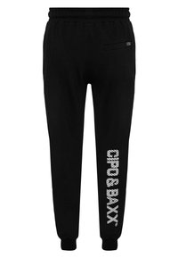 Schwarze Baumwoll-Jogginghose mit elastischem Bund, ausgestattet mit einer Seitentasche und einem weißen Textdruckdesign entlang des linken Beins.