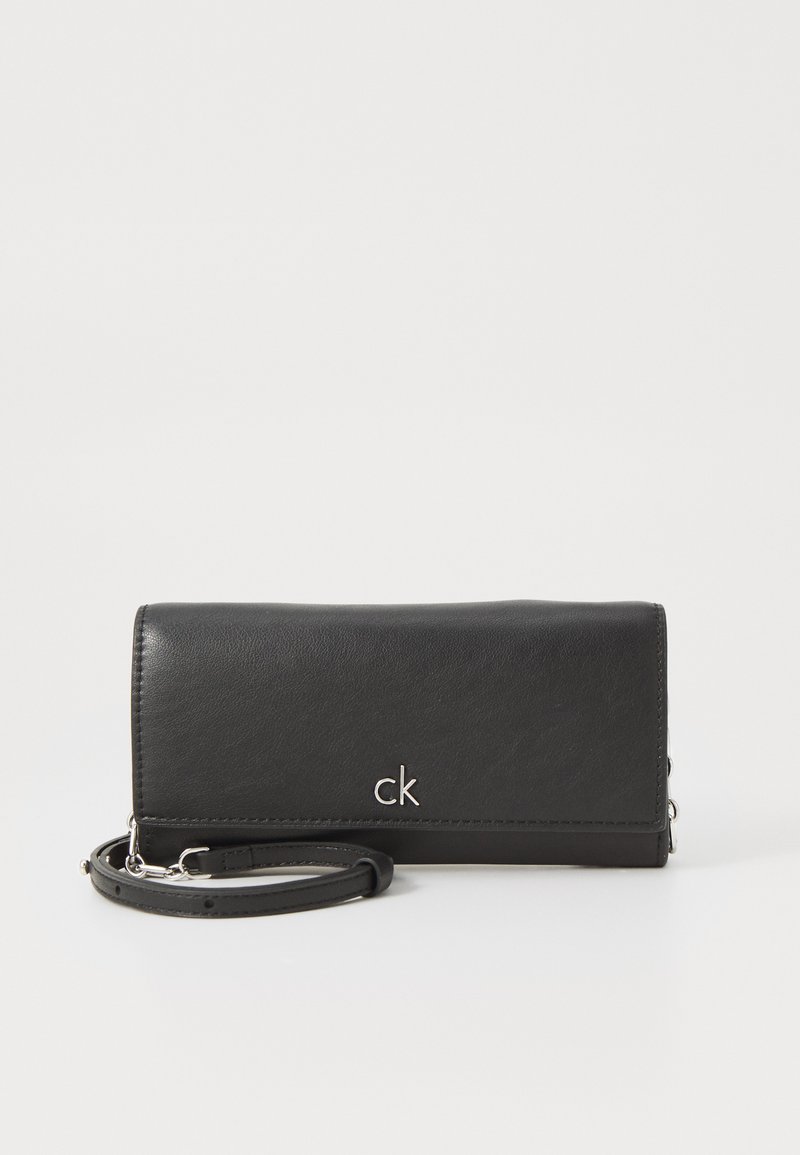 Musta nahkainen lompakko rannekkeen kanssa, hopeinen logo, suorakaiteen muotoinen, sileä pinta, vetoketjulla suljettava, minimalistinen muotoilu.