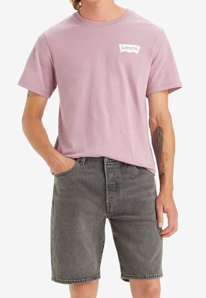 T-shirt di cotone rosa chiaro con logo bianco Levi's sul lato sinistro del petto, abbinata a pantaloni di denim grigi. Collo rotondo semplice e maniche corte.