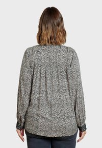 Blusa a maniche lunghe in stampa floreale crema e nera, con schiena arricciata e polsini elasticizzati. Tessuto morbido con una vestibilità rilassata.