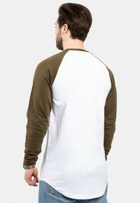 Hosszú ujjú raglan póló, olajzöld ujjal és fehér testtel, puha pamutból készült, ívelt hátú hemnyereggel.