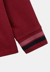 Poignet de chemise à manches longues bourgogne avec des rayures horizontales en rose, bleu foncé et rouge. Texture douce avec un design ajusté.