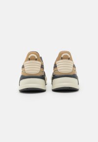 Zapatillas deportivas marrones y grises con un upper de malla texturizada, soporte acolchado en el talón y una suela blanca gruesa. Diseñadas para la comodidad y la estabilidad.