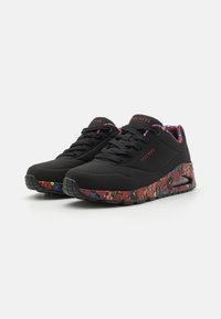 Baskets de sport noires avec une tige texturée, arborant un motif floral coloré sur la semelle et un collier rembourré pour le confort.