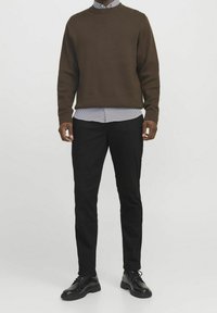 Brązowy, teksturowany sweter typu pulower na niebiesko-białej, paskowanej koszuli, w zestawieniu z czarnymi, dopasowanymi spodniami i czarnymi skórzanymi butami.