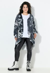 Zwart-witte tie-dye lange cardigan over een wit shirt, gecombineerd met zwarte glanzende leggings en zilveren veterschoenen. Glad materiaal, comfortabele pasvorm.