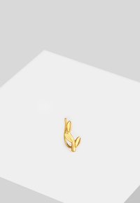 Pendiente de color dorado en forma de tallo de planta con dos pequeñas hojas. La textura suave y el intrincado detalle realzan su aspecto orgánico.
