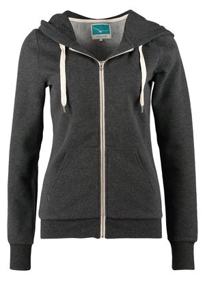 Personne marchant vers l'avant portant un sweat à capuche noir, un débardeur blanc, un jean skinny bleu, des baskets grises et un sac à dos noir.