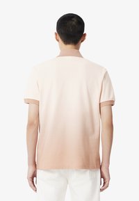 Vaaleanpunainen polo-paita, jossa on liukuväri-efekti, lyhyet hihat ja kontrastivärinen kaulus. Sileä kangas ja rento malli on suunniteltu mukavuutta varten.