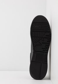 Black rubber shoe sole with textured patterns, including vertical and horizontal lines, logo imprint, and a rounded toe design.