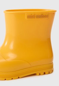 Bottes de pluie pour enfants jaunes et brillantes, avec une semelle texturée et "mini melissa" embossé sur la zone de la cheville.