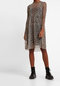 Leopardenmuster-Kleid aus durchscheinendem Material mit langen Ärmeln, gerafftem Taillenbund und knielangem Saum, kombiniert mit schwarzen Schnürstiefeln bis zum Knöchel.