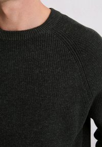 Dunkelgrüner gerippter Strickpullover mit rundem Ausschnitt und Raglanärmeln, der einen strukturierten Stoff und subtile Farbvariationen zeigt.
