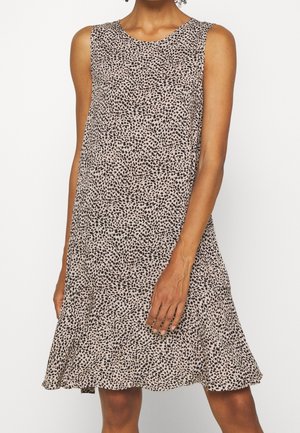 Robe beige sans manches avec des points noirs irréguliers, coupe ample, longueur au genou, portée par une personne debout sur un fond blanc uni.