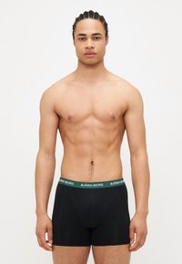 Boxer-culottes noires avec une ceinture verte arborant le logo "BJÖRN BORG", présentant un design ajusté et une texture douce.