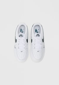 Bijele Nike Air Force 1 tenisice s crnim detaljima, teksturirani gornji dio, perforirani vrh i bijele vezice. Logo prikazan na jeziku i sa strane.