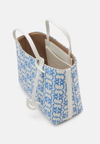 Sac cabas à motifs bleus et blancs avec des poignées en cuir blanc, une poche intérieure et un pendentif logo en cuir blanc suspendu.