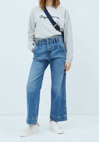 Felpa grigia chiara con scritte navy, jeans a vita alta blu in denim a gamba larga e sneakers bianche. Tessuto morbido e vestibilità casual.