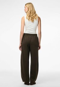 Débardeur gris clair et un pantalon de survêtement large marron foncé avec une taille élastique, vus de dos. Texture du tissu lisse et douce.