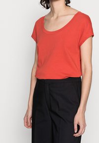 Rød bomulds T-shirt med rund halsudskæring og korte ærmer, parret med højtaljede sorte bukser. Simple design og glat tekstur.