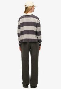 Stripet, grå og mørkegrøn sweatshirt med krave, parret med løse mørkegrønne bukser og en beige kasket.
