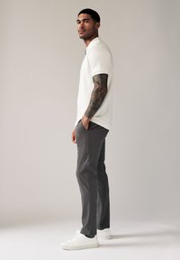 Polo shirt in white, slim fit, paired with dark gray trousers and white sneakers. Features a textured material and fitted design.