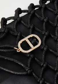 Sac en tissu noir avec un design en corde tissée noire, doté d'une fermeture accentuée de doré et de cristaux. Détails texturés et complexes.