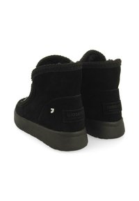 Botines de ante negro con un puño texturizado, que cuentan con una suela de goma plana y un parche con el logo en la parte trasera. Diseño simple y funcional.