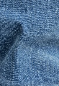 Modrá denímová tkanina s texturovanou vazbou, vykazující jemné variace v odstínu a měkký, mírně elastický povrch. Bez výrazných vzorů nebo akcentů.